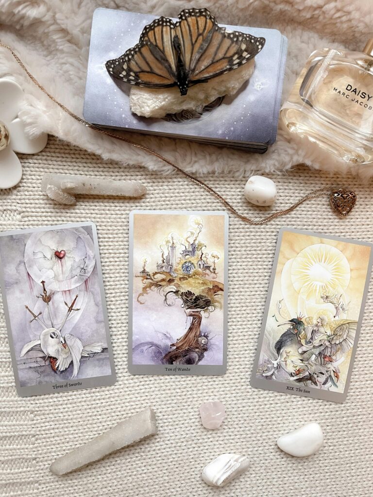 Aesthetic flatlay featuring tarot cards, a butterfly, and perfume on textured fabric.